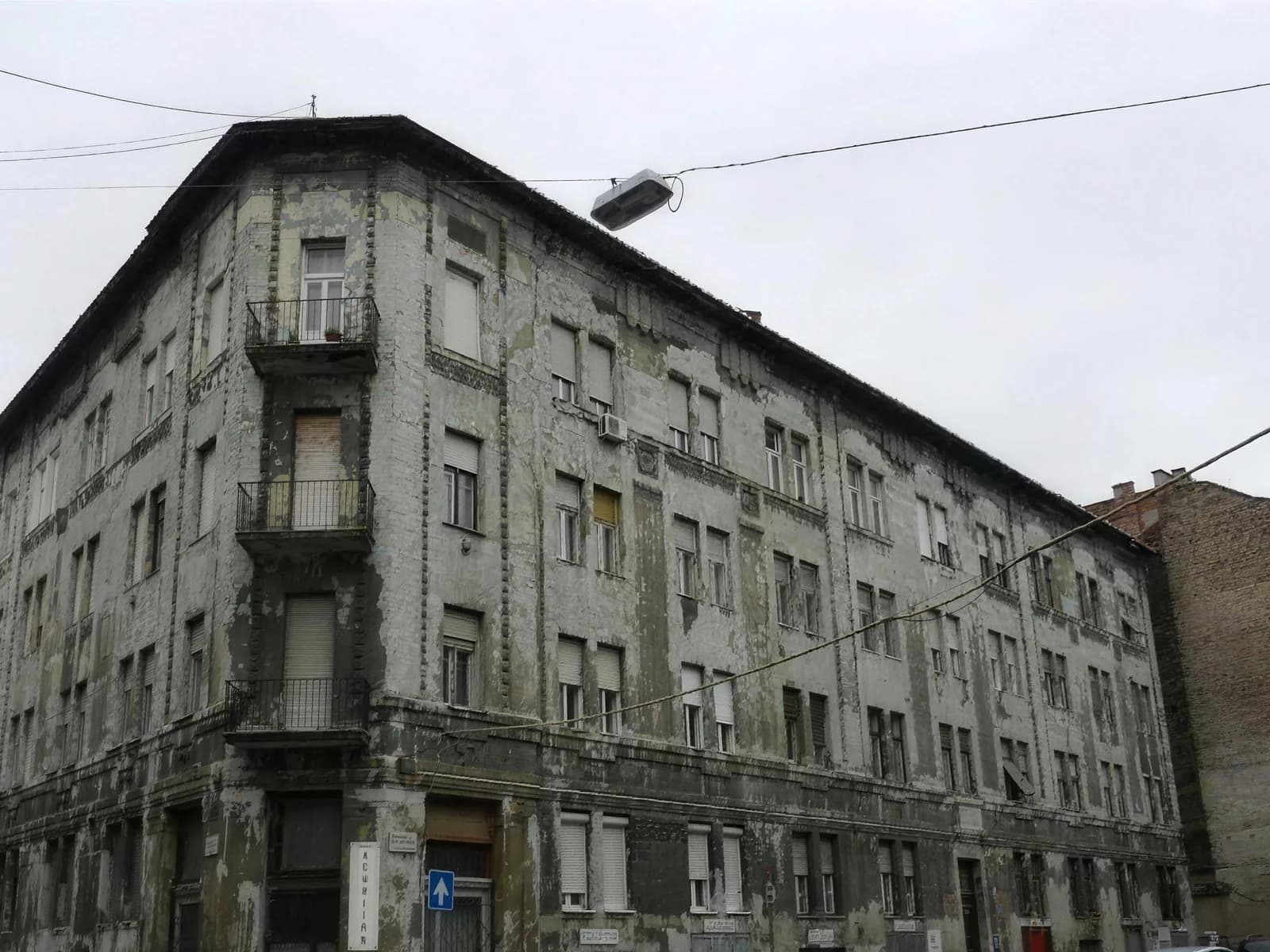 Leromlott állapotú budapesti sarokház szürke, málló homlokzattal a felújítás előtt